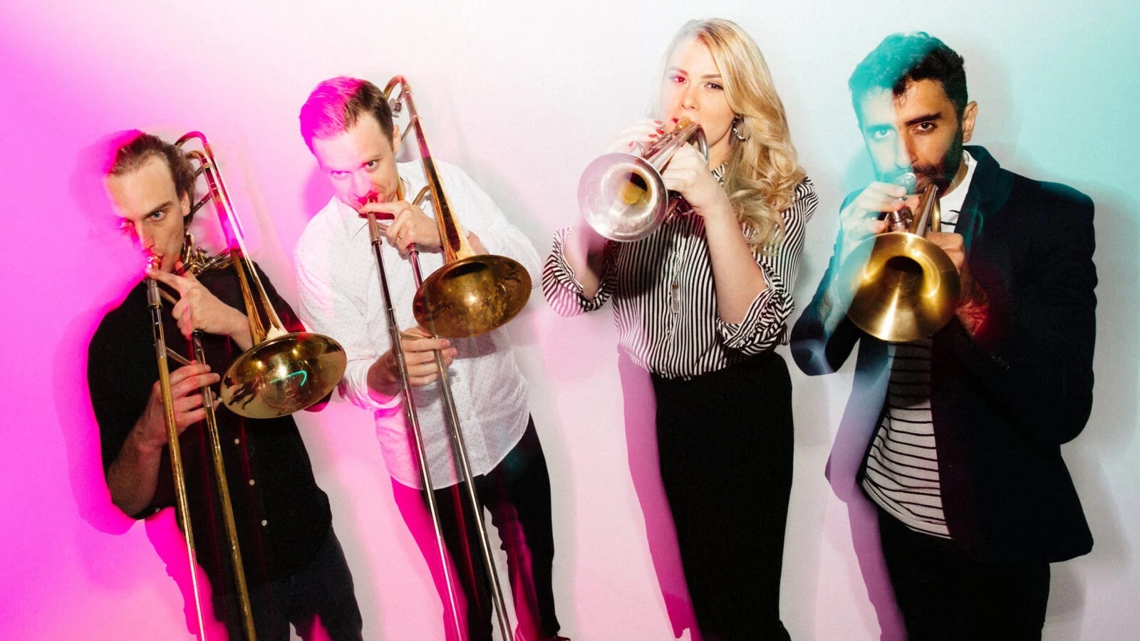 Four brass players in motion cast in pink and green lights